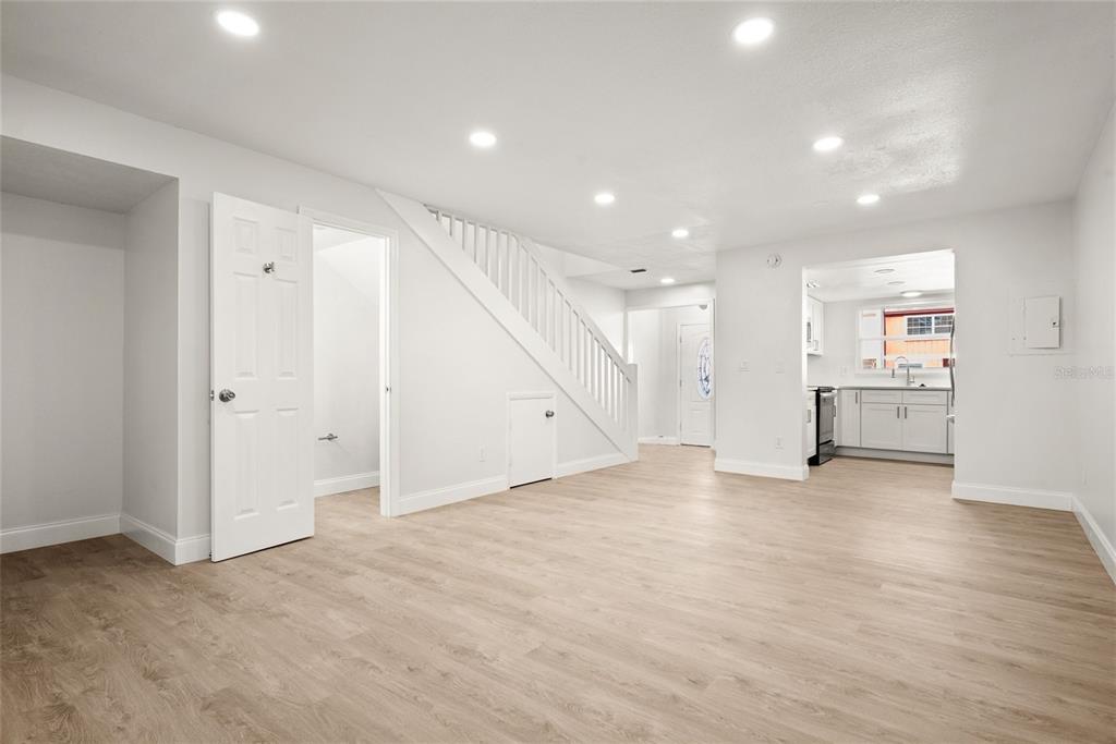 A bright, open-concept living area with light wood flooring, white walls, and a staircase — 3150 S PINES DRIVE UNIT 84, LARGO, FL