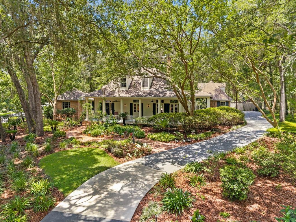A two-story house with a wrap-around porch sits behind a curved driveway and landscaped yard — 9326 SW 53RD LANE, GAINESVILLE, FL