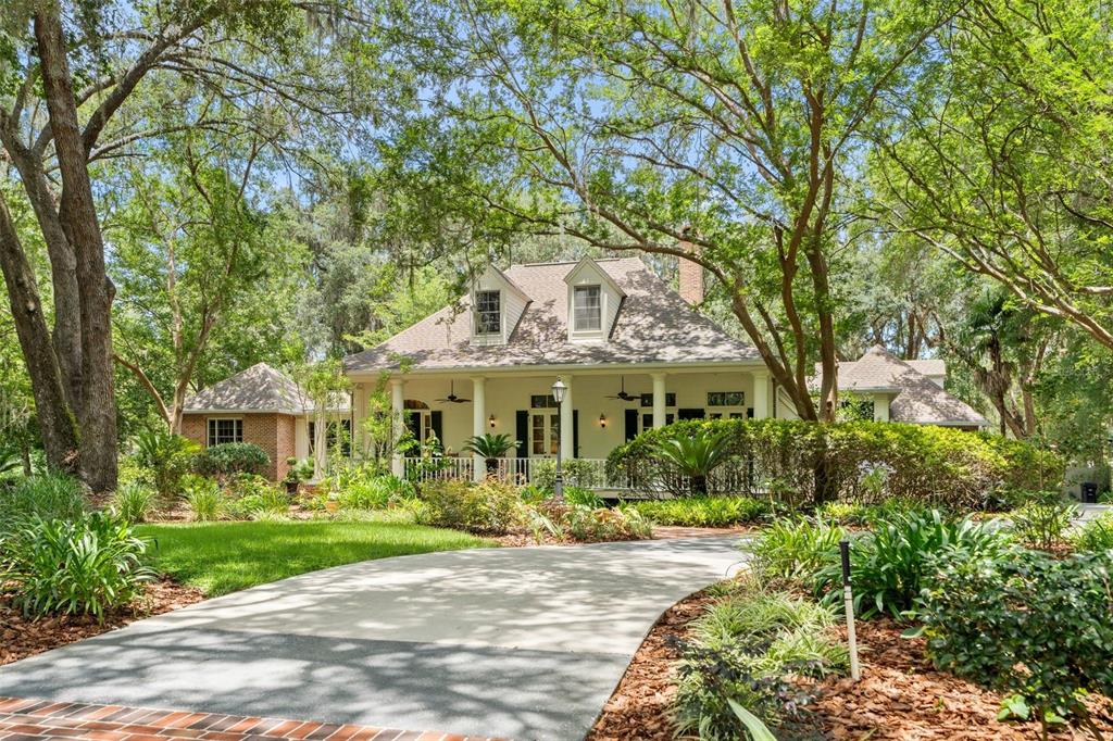 A concrete driveway leads to a white house with a covered porch and dormer windows — 9326 SW 53RD LANE, GAINESVILLE, FL
