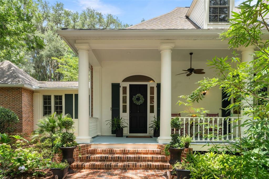 A brick-fronted house features a covered porch with white columns and a black front door — 9326 SW 53RD LANE, GAINESVILLE, FL