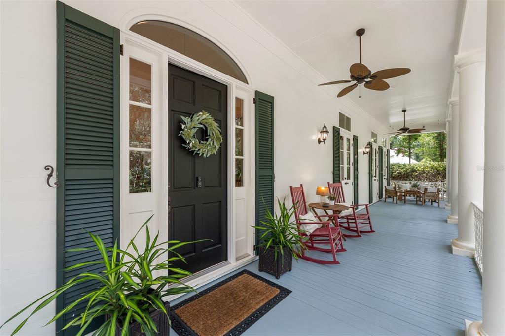 A covered porch features a black front door, green shutters, and red rocking chairs — 9326 SW 53RD LANE, GAINESVILLE, FL