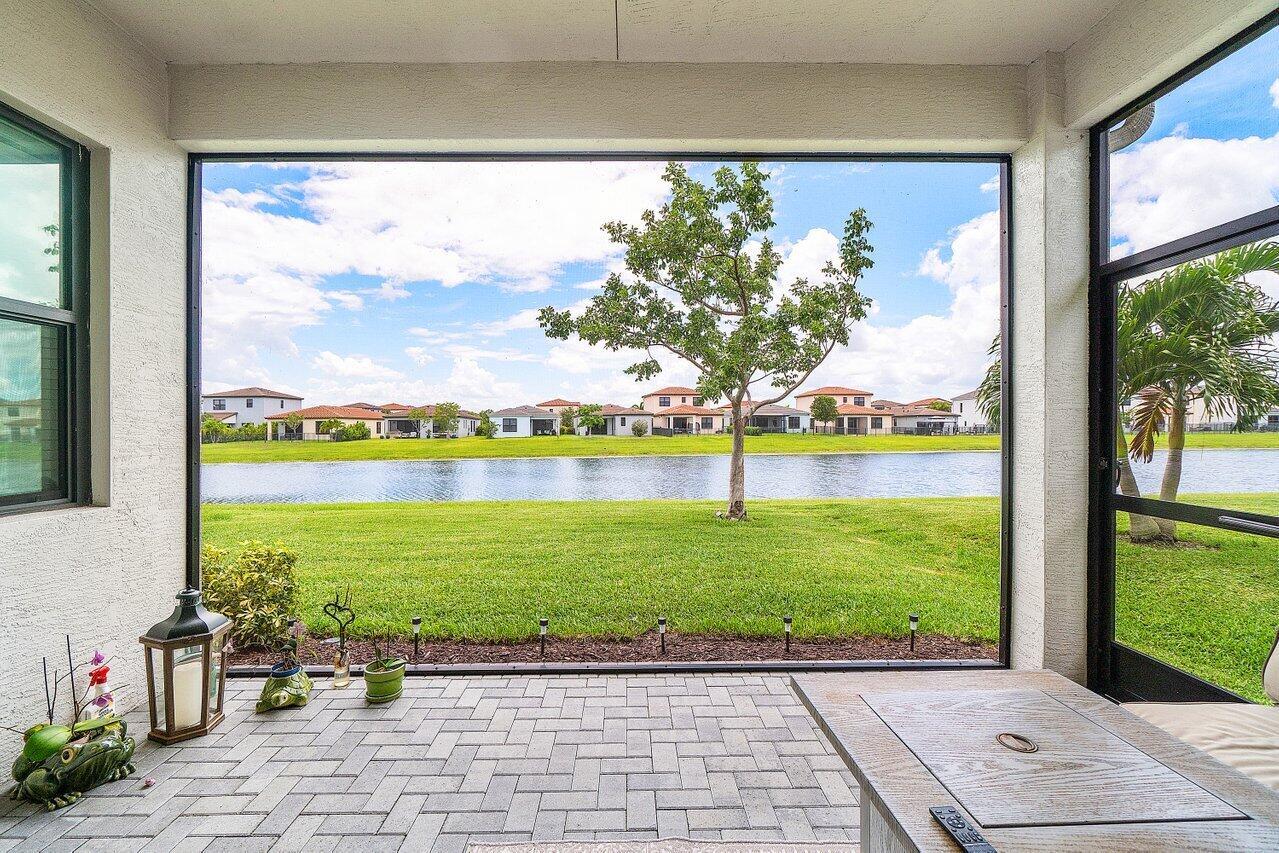 A screened-in patio with brick pavers overlooks a grassy lawn, a pond, and distant houses — 16070 Key Biscayne Lane, Westlake FL 33470, WESTLAKE, FL