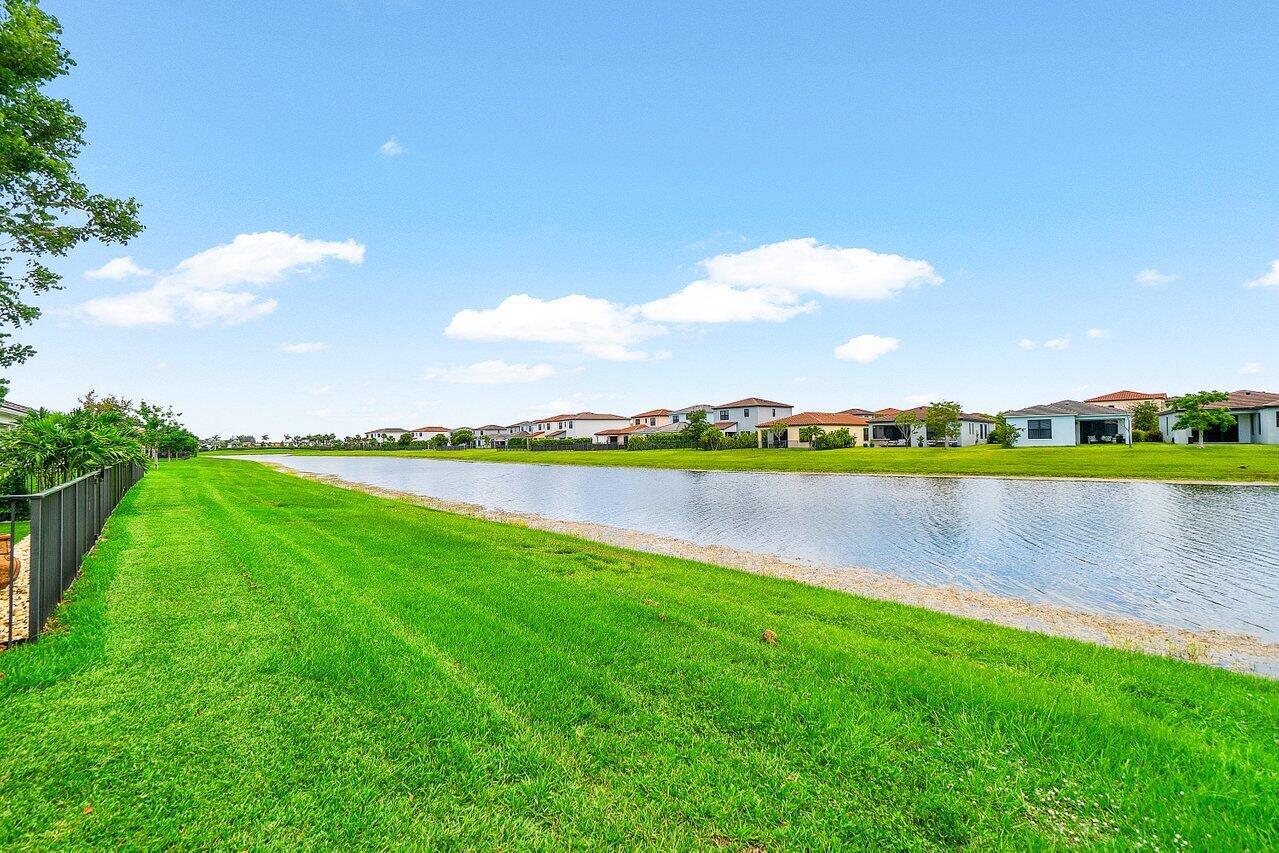 A grassy backyard overlooks a long, narrow pond with residential houses in the background — 16070 Key Biscayne Lane, Westlake FL 33470, WESTLAKE, FL