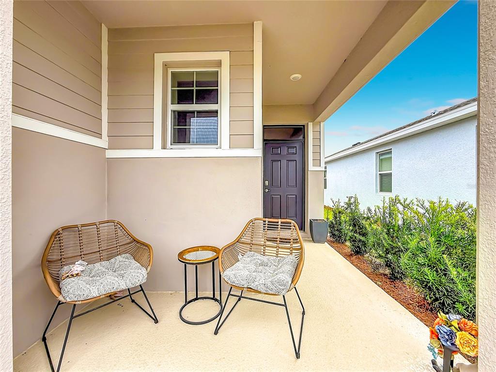 A covered porch features two wicker chairs, a small side table, and a dark front door — 4143 NW 44TH CIRCLE, OCALA, FL