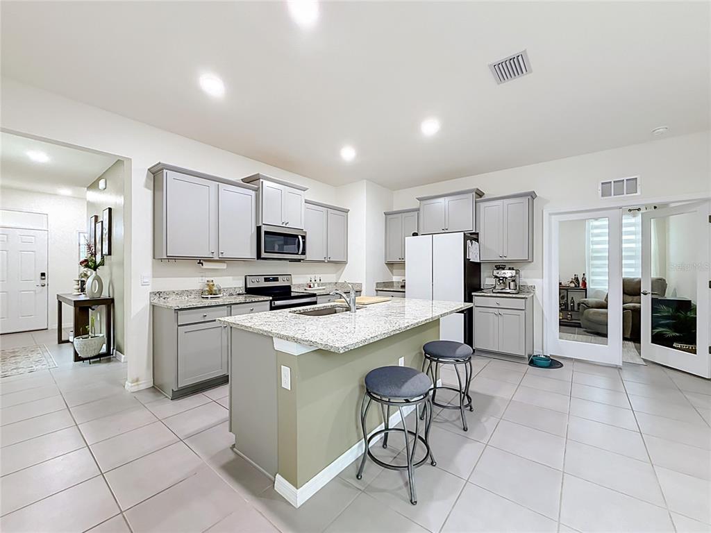 A kitchen features gray cabinets, granite countertops, a central island with stools, and tile flooring — 4143 NW 44TH CIRCLE, OCALA, FL