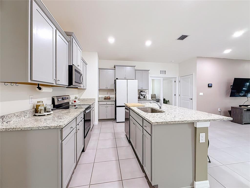 A kitchen features gray cabinets, granite countertops, a central island, and light-colored tile flooring — 4143 NW 44TH CIRCLE, OCALA, FL