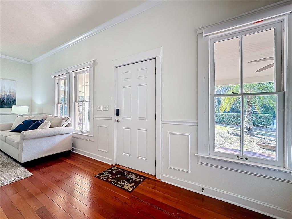 A living room features white walls, wainscoting, hardwood floors, a front door, and large windows — 1148 N GRANDVIEW STREET, MOUNT DORA, FL