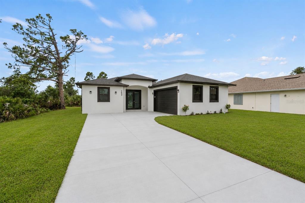 A single-story house with a white stucco exterior, dark trim, and a concrete driveway — 153 AUSTRALIAN DRIVE, ROTONDA WEST, FL