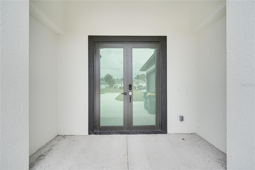 A covered concrete entryway features a set of double glass doors with dark frames — 153 AUSTRALIAN DRIVE, ROTONDA WEST, FL