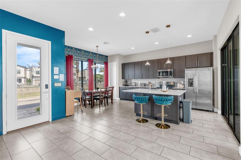 A modern kitchen features dark wood cabinets, a white island with blue stools, and tile flooring — 415 VILLA DOMANI WAY, DAVENPORT, FL
