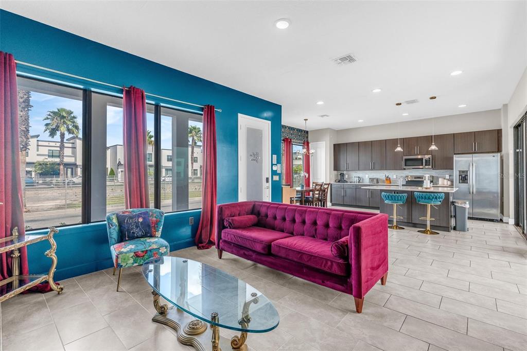 A living room with a magenta sofa, blue accent wall, and an open-concept kitchen — 415 VILLA DOMANI WAY, DAVENPORT, FL