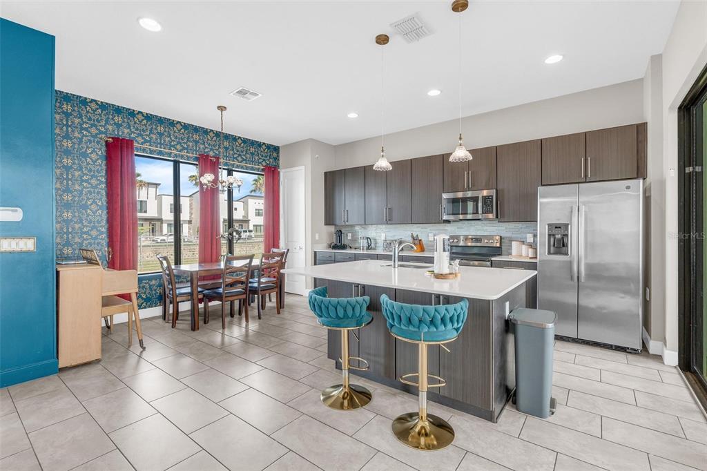 A kitchen with dark cabinets, a white island, and a dining area with patterned wallpaper — 415 VILLA DOMANI WAY, DAVENPORT, FL