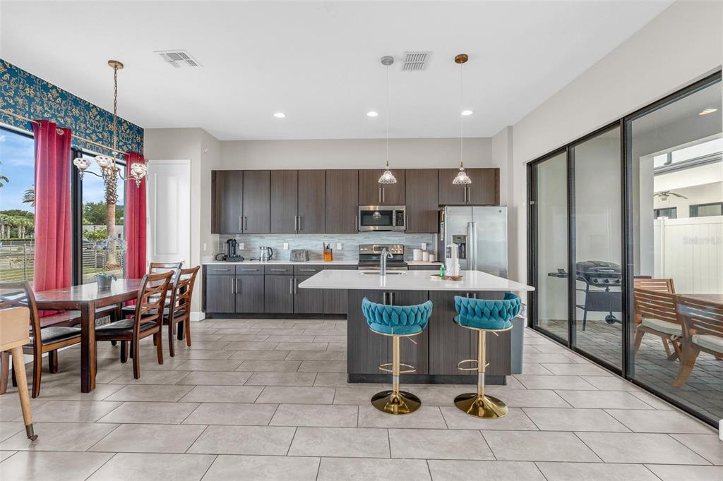 A modern kitchen features dark wood cabinetry, a central island with blue stools, and tile flooring — 415 VILLA DOMANI WAY, DAVENPORT, FL