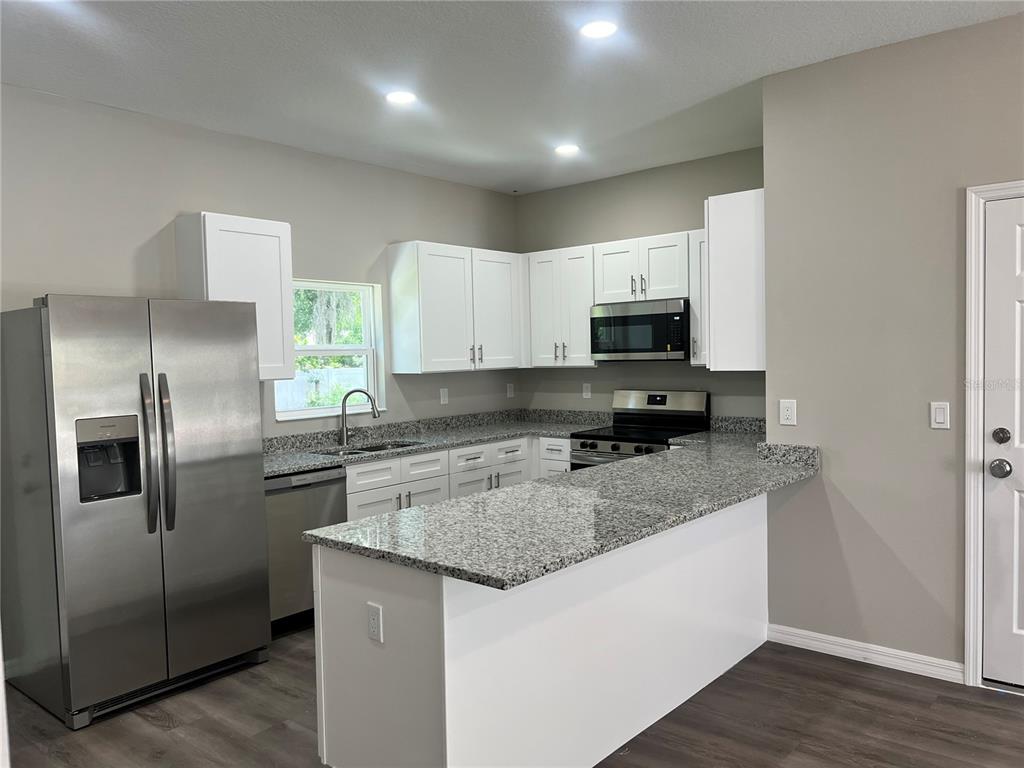 A kitchen features white cabinets, granite countertops, stainless steel appliances, and dark wood-look flooring — 5008 FINDERS COURT, TAMPA, FL
