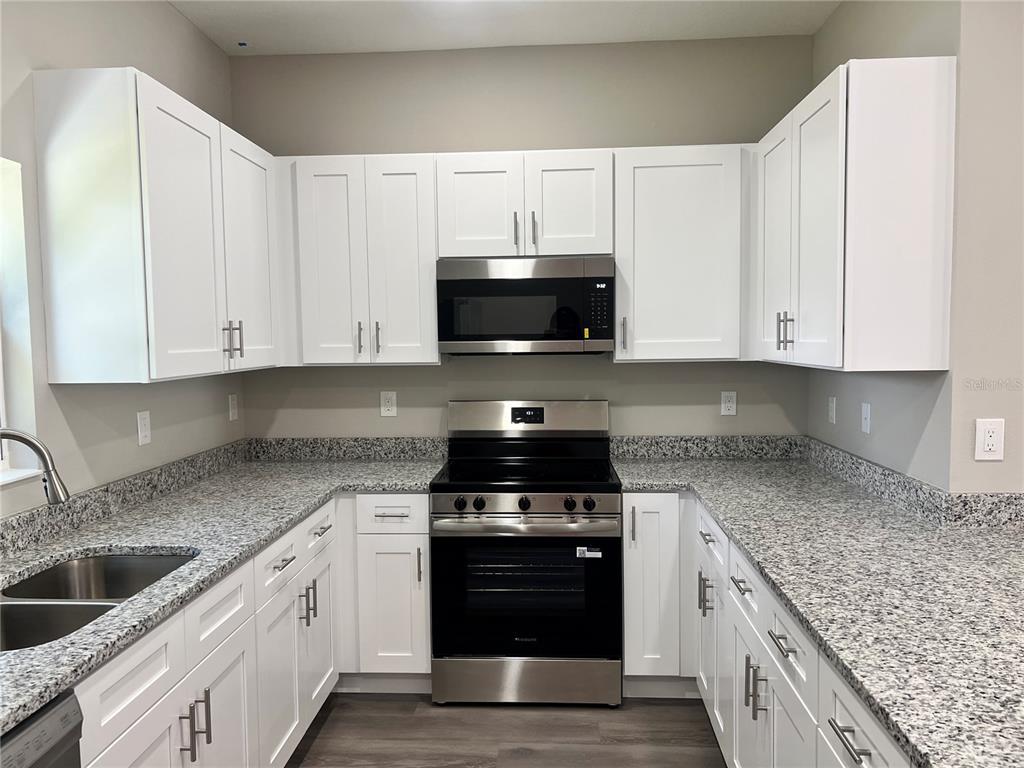 A kitchen features white cabinets, granite countertops, and stainless steel appliances — 5008 FINDERS COURT, TAMPA, FL