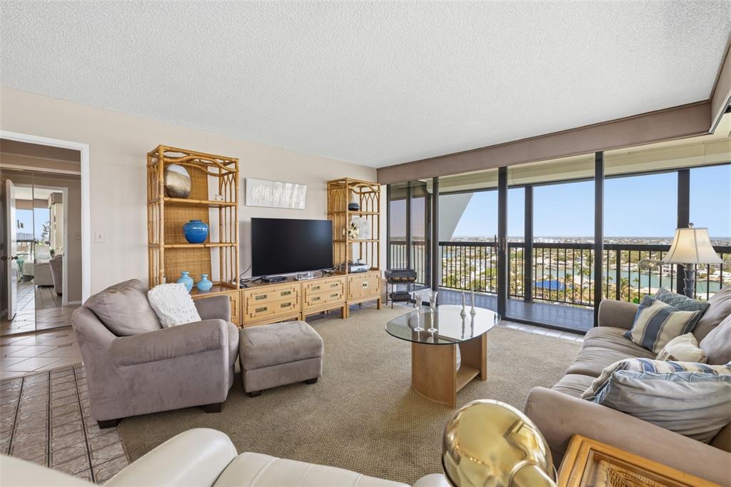 A living room features wicker shelving, a television, a glass coffee table, and a balcony view — 9495 BLIND PASS ROAD UNIT 1208, ST PETE BEACH, FL