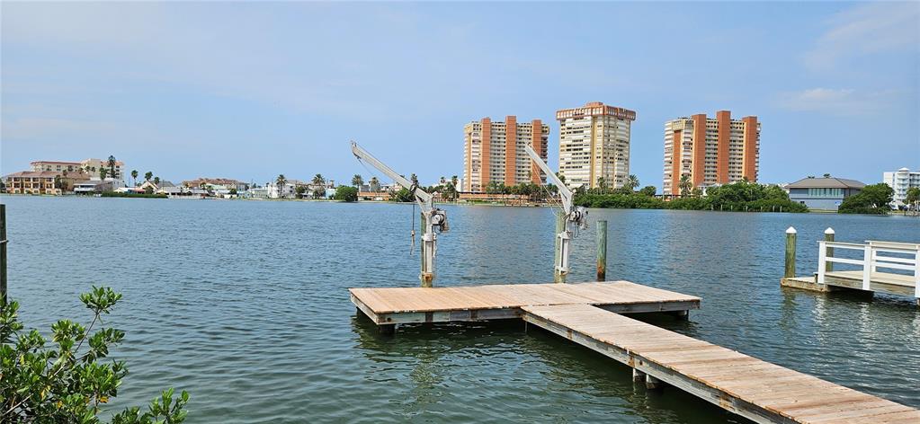 A wooden dock with two boat lifts extends into a calm bay near high-rise buildings — 623 180TH AVENUE E, REDINGTON SHORES, FL