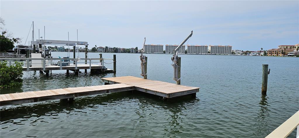 A wooden dock with two boat lifts extends into a calm bay — 623 180TH AVENUE E, REDINGTON SHORES, FL