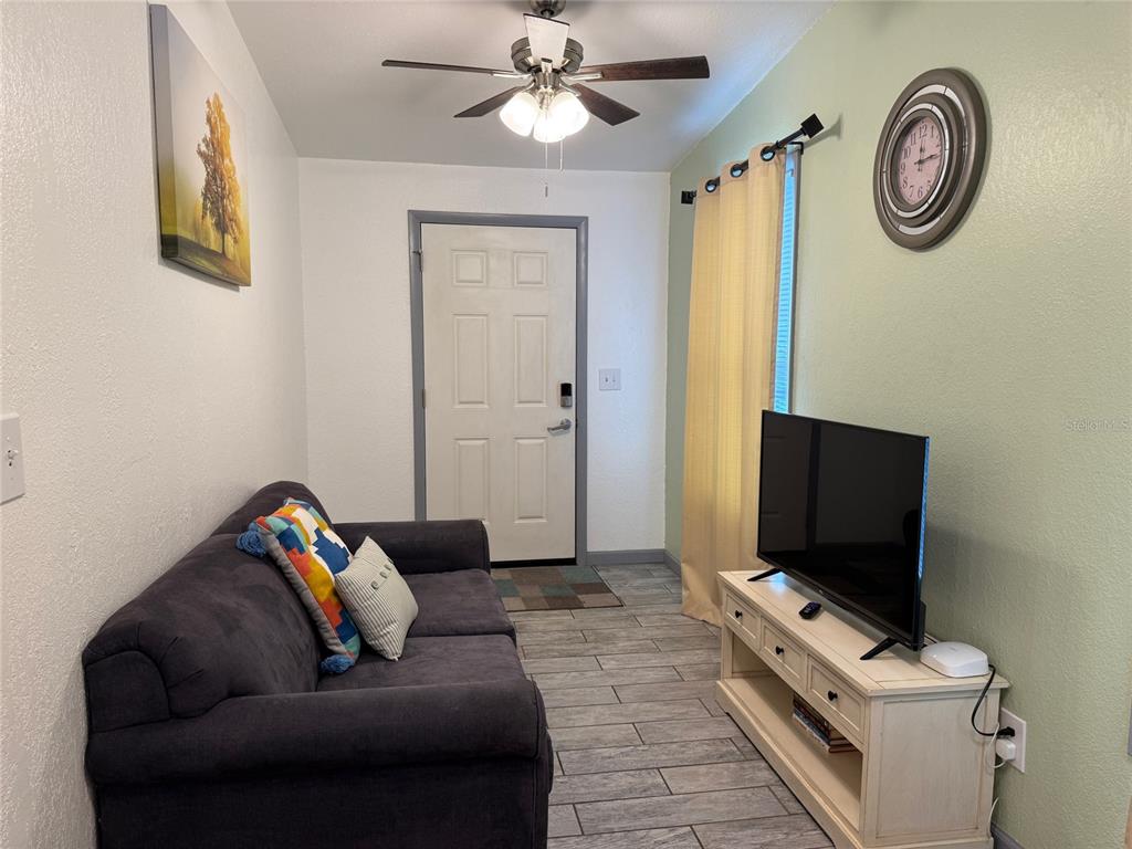A living room features a dark sofa, a television on a white stand, and tile flooring — 907 N WABASH AVE, LAKELAND, FL