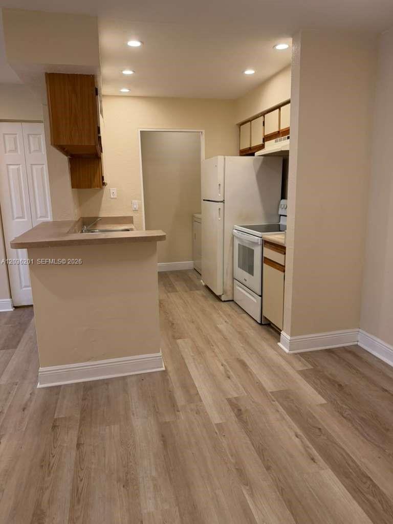 A kitchen features light-colored walls, wood-look flooring, white appliances, and a breakfast bar — 1247 SW 46th Ave # 1306, Pompano Beach FL 33069, POMPANO BEACH, FL