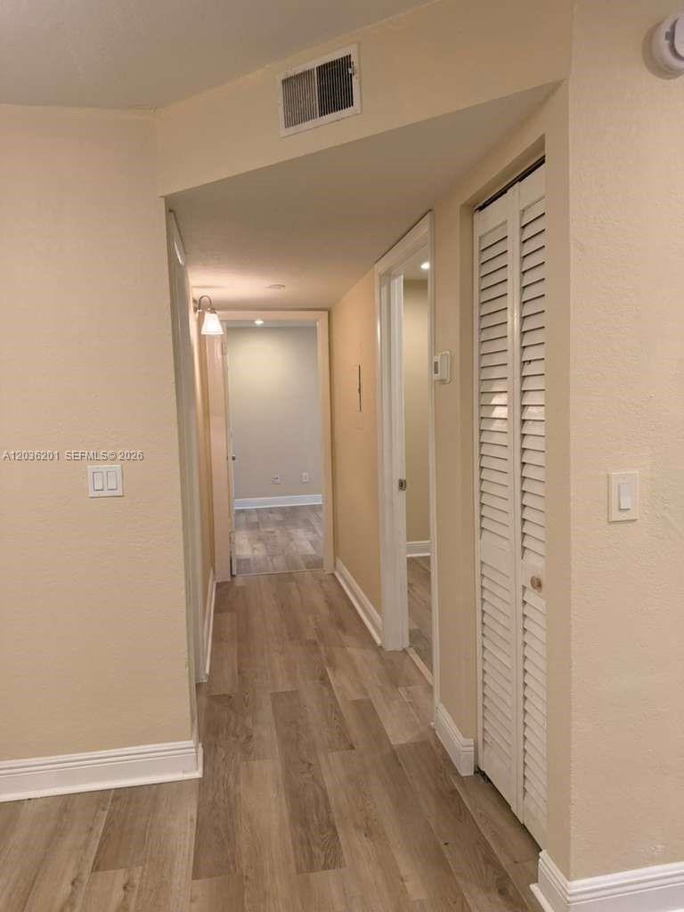 A hallway with light-colored walls, wood-look flooring, and white louvered closet doors — 1247 SW 46th Ave # 1306, Pompano Beach FL 33069, POMPANO BEACH, FL