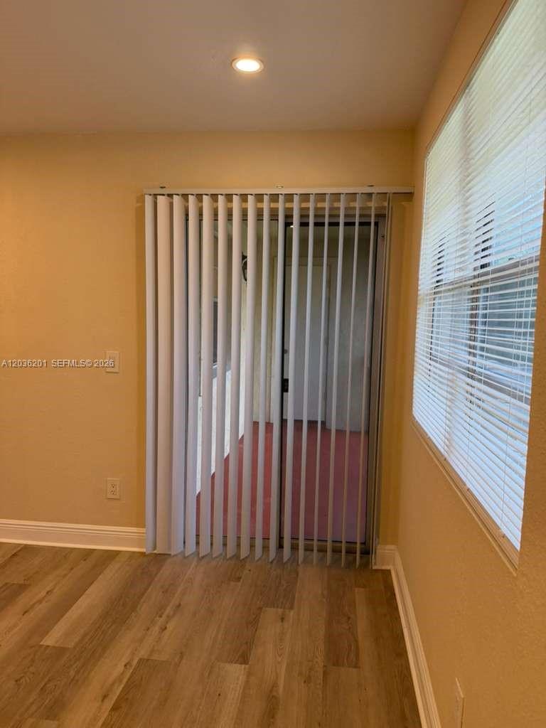 A room with wood-look flooring, vertical blinds over a sliding door, and a window — 1247 SW 46th Ave # 1306, Pompano Beach FL 33069, POMPANO BEACH, FL