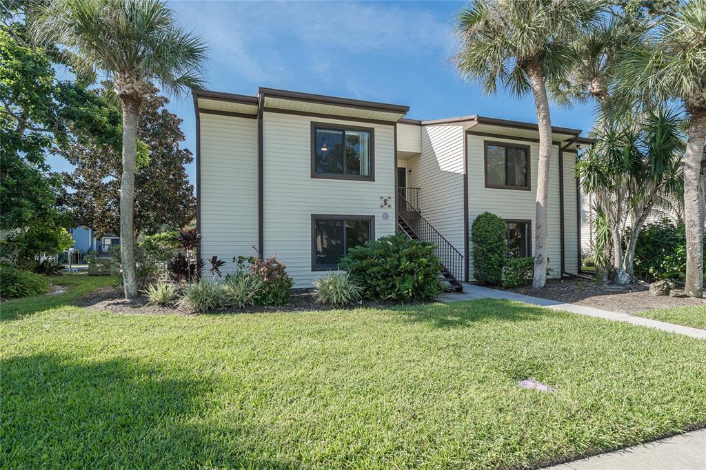 A two-story apartment building with beige siding, palm trees, and a front lawn — 372 MOORINGS COVE DRIVE UNIT 372, TARPON SPRINGS, FL