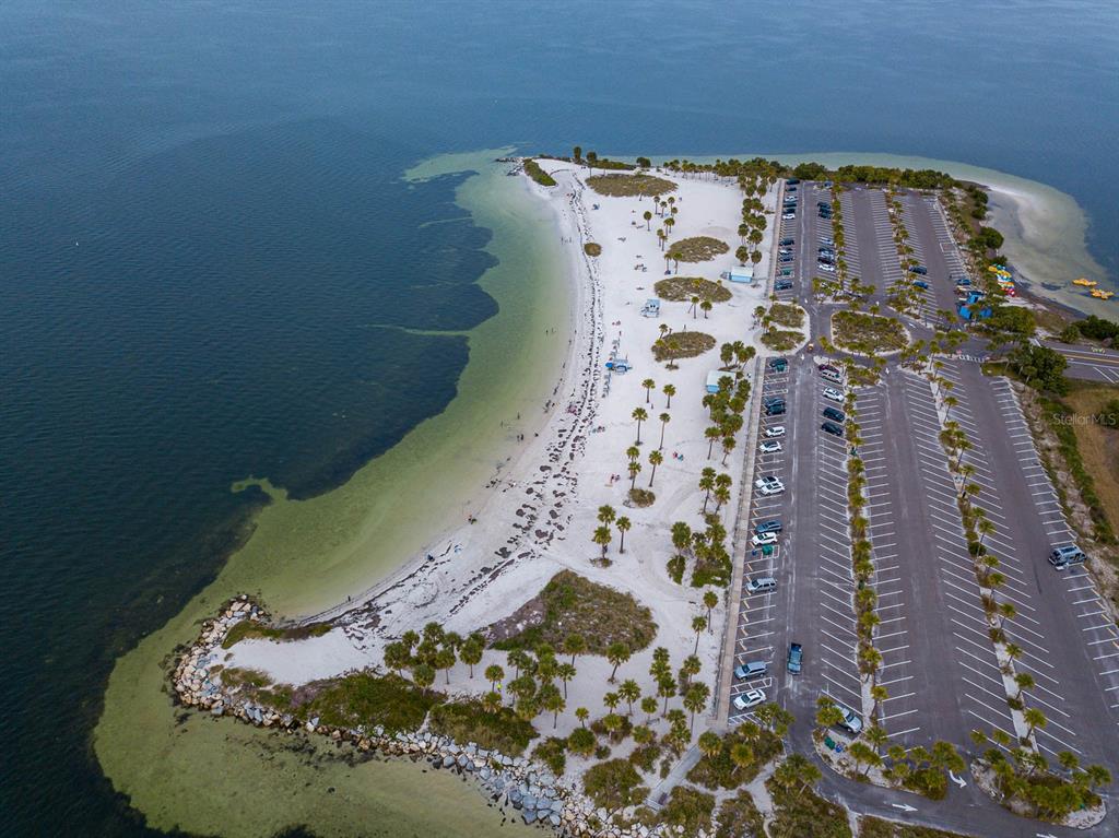 Aerial view of a sandy beach, palm trees, and a large parking lot by water — 372 MOORINGS COVE DRIVE UNIT 372, TARPON SPRINGS, FL
