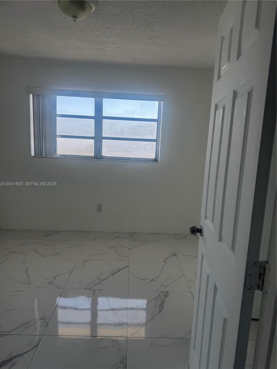 An empty room features white walls, a window with blinds, and white marble-patterned tile flooring — 1551 W Okeechobee Rd # 19, Hialeah FL 33010, HIALEAH, FL