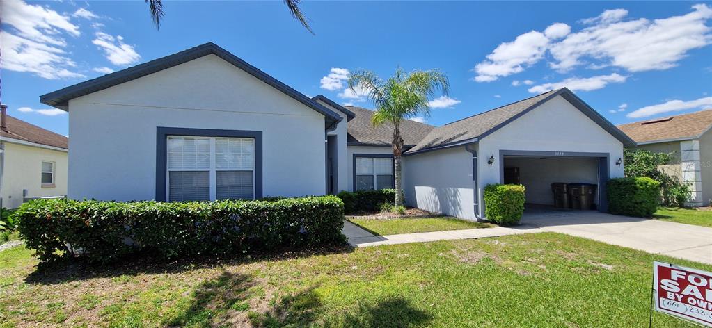 A single-story house with a light-colored exterior, a two-car garage, and a manicured hedge — 5344 CORAL VINE LANE, KISSIMMEE, FL