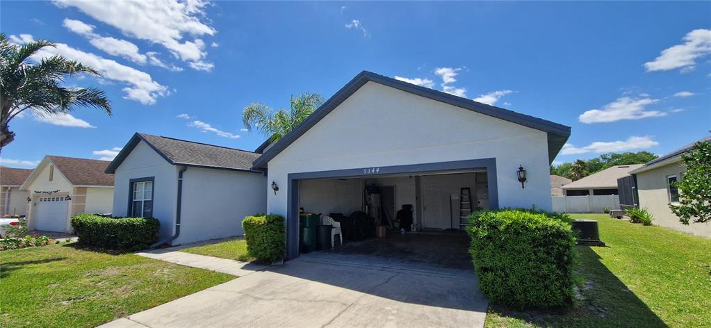 A single-story house features a two-car garage, a concrete driveway, and a manicured lawn — 5344 CORAL VINE LANE, KISSIMMEE, FL