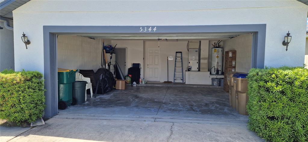 An open garage with concrete floors, storage items, a water heater, and an HVAC unit — 5344 CORAL VINE LANE, KISSIMMEE, FL