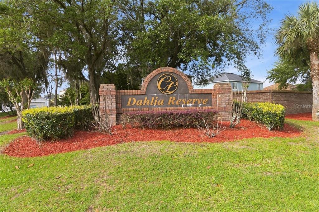 A brick monument sign for Dahlia Reserve sits in a landscaped yard with trees — 5344 CORAL VINE LANE, KISSIMMEE, FL