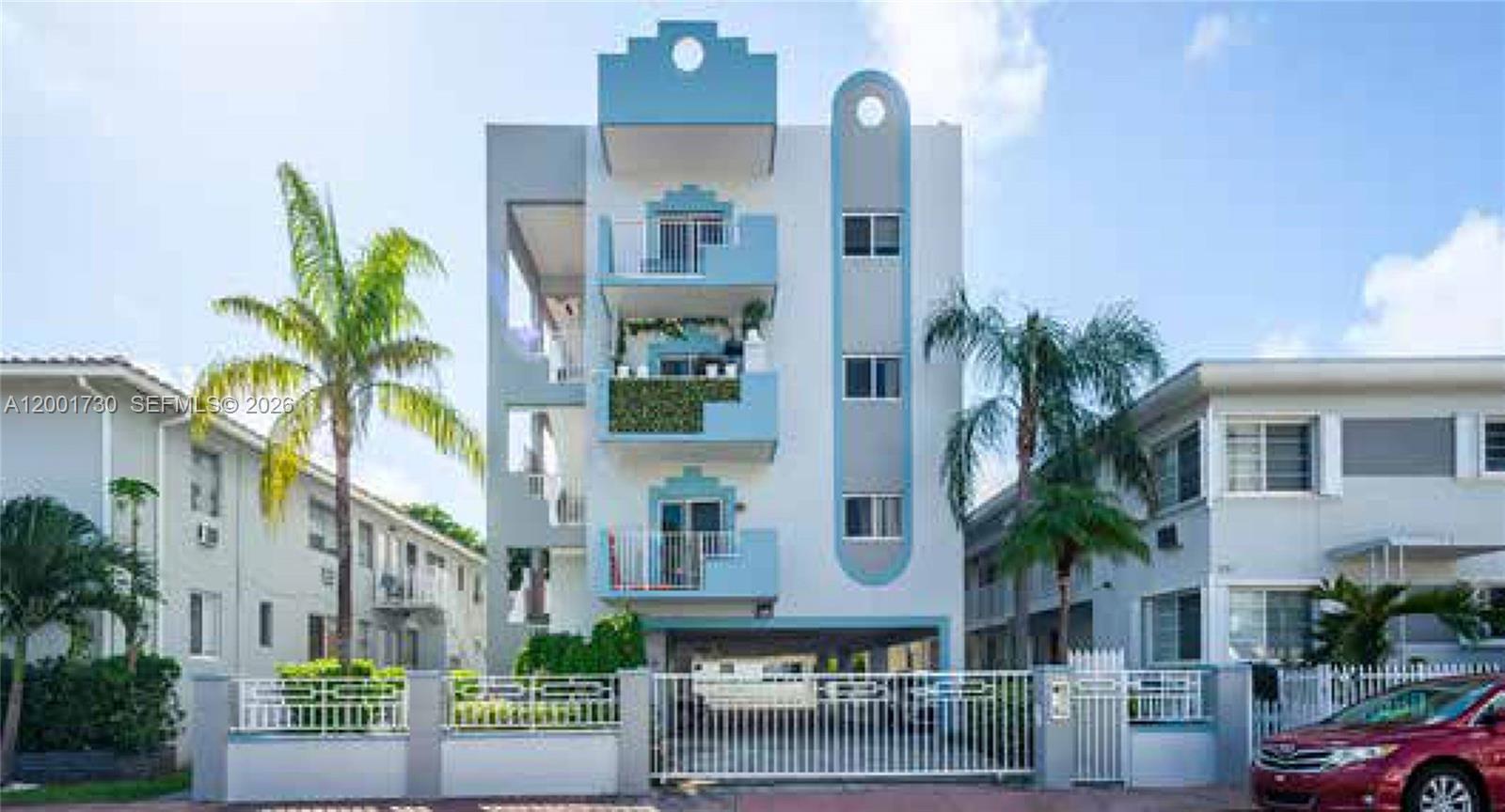 A four-story apartment building with blue accents and balconies stands behind a white fence — 709 83rd St, Miami Beach FL 33141, MIAMI BEACH, FL