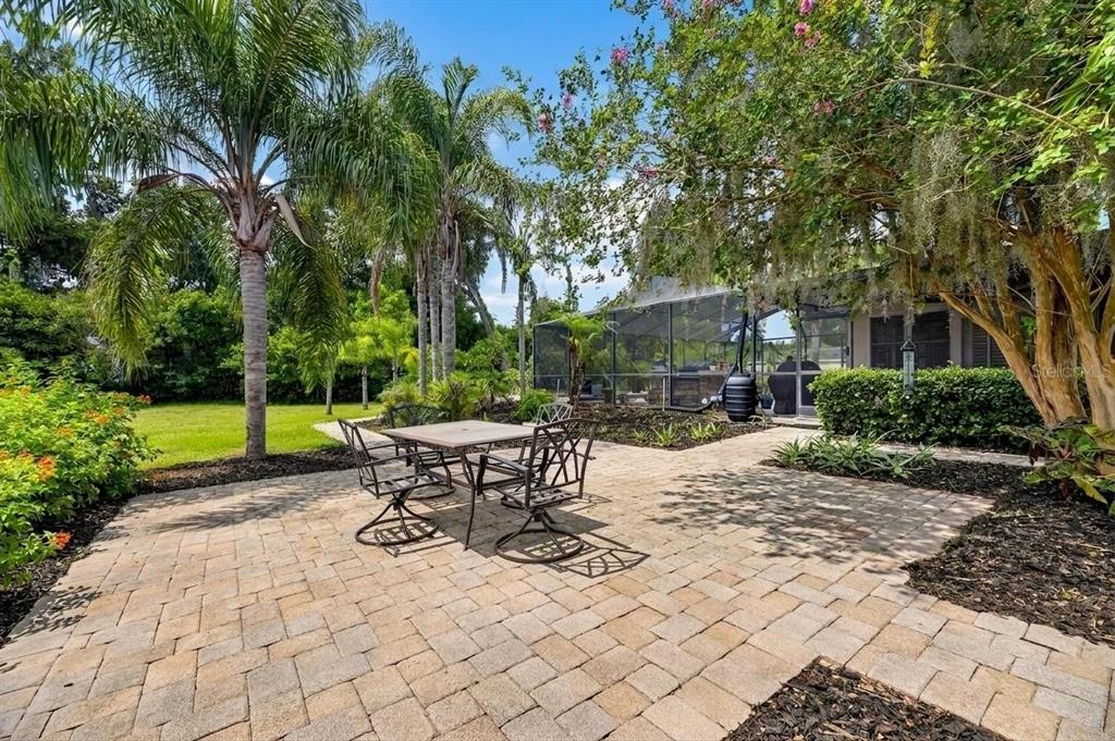 A paved patio with a dining set sits outside a screened-in pool enclosure and garden — 2715 LITTLE ROAD, VALRICO, FL