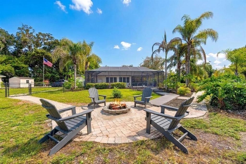 A backyard features a circular stone fire pit surrounded by four chairs on a patio — 2715 LITTLE ROAD, VALRICO, FL