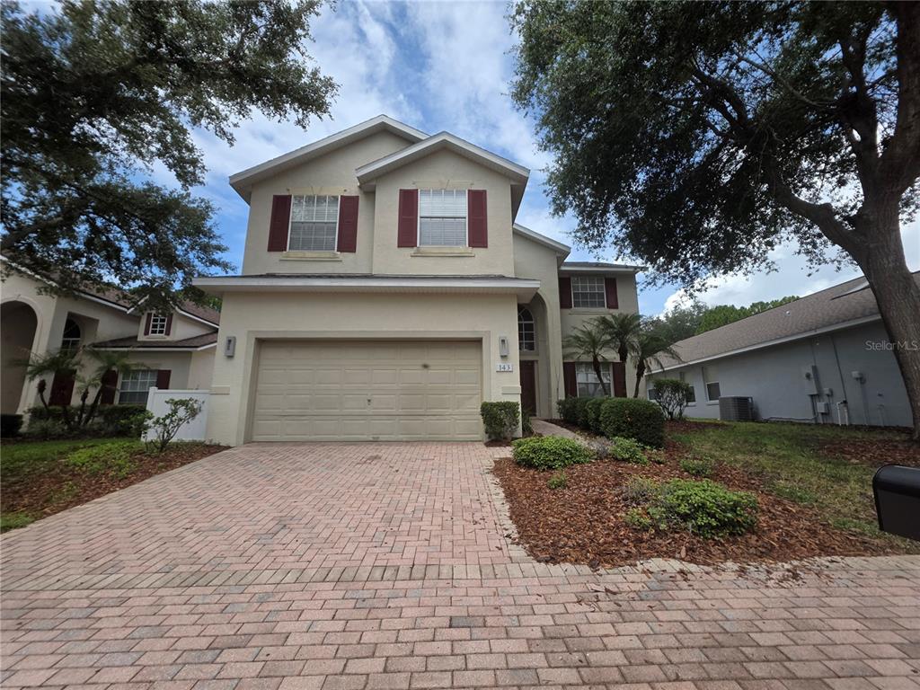 A two-story house features a tan stucco exterior, a two-car garage, and a brick driveway — 143 E WINDSOR PLACE, DAVENPORT, FL