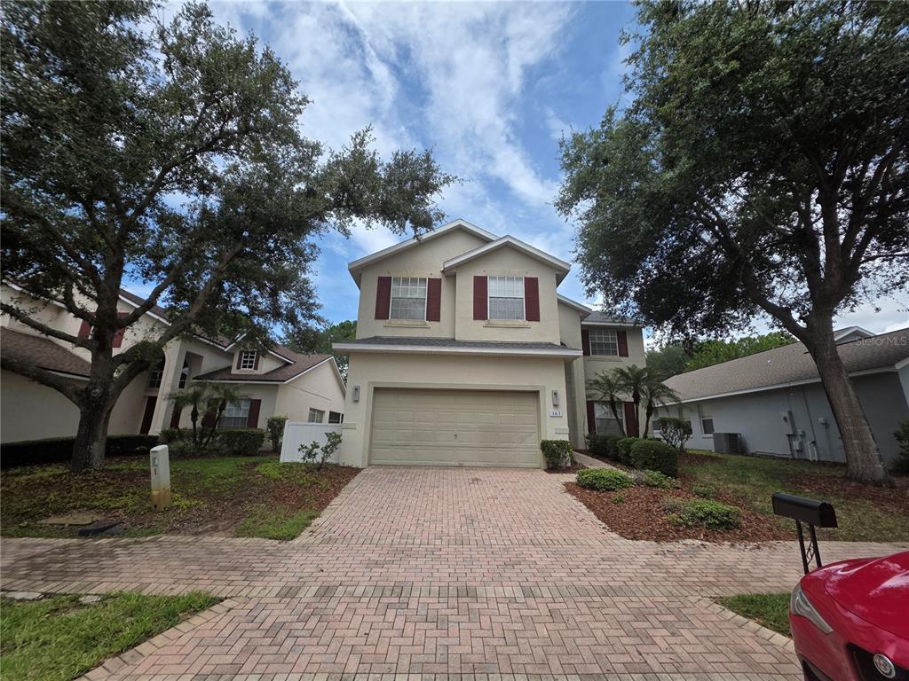 A two-story house with a beige stucco exterior, a two-car garage, and a brick driveway — 143 E WINDSOR PLACE, DAVENPORT, FL