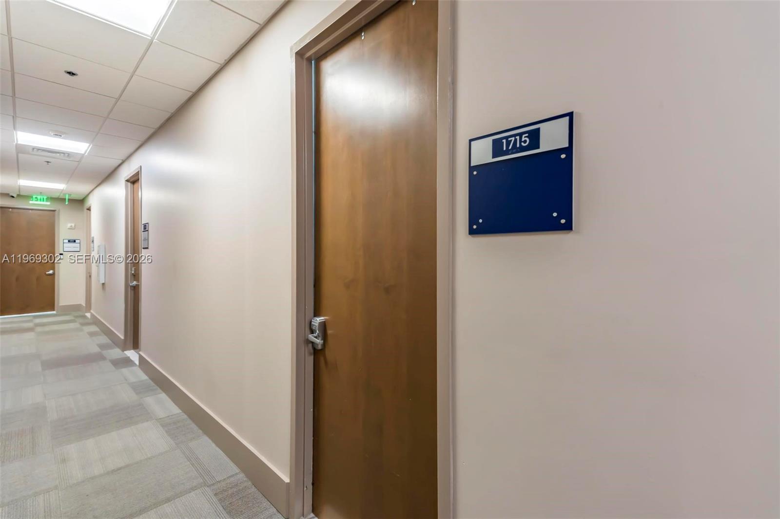 A hallway features a wooden door labeled 1715, beige walls, and carpeted flooring — 175 SW 7th St # 1715, Miami FL 33130, MIAMI, FL