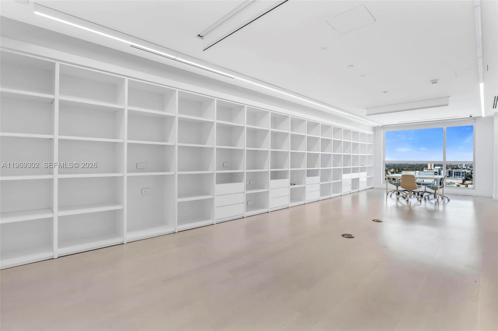A bright office space features a long wall of white built-in shelving and floor-to-ceiling windows — 175 SW 7th St # 1715, Miami FL 33130, MIAMI, FL