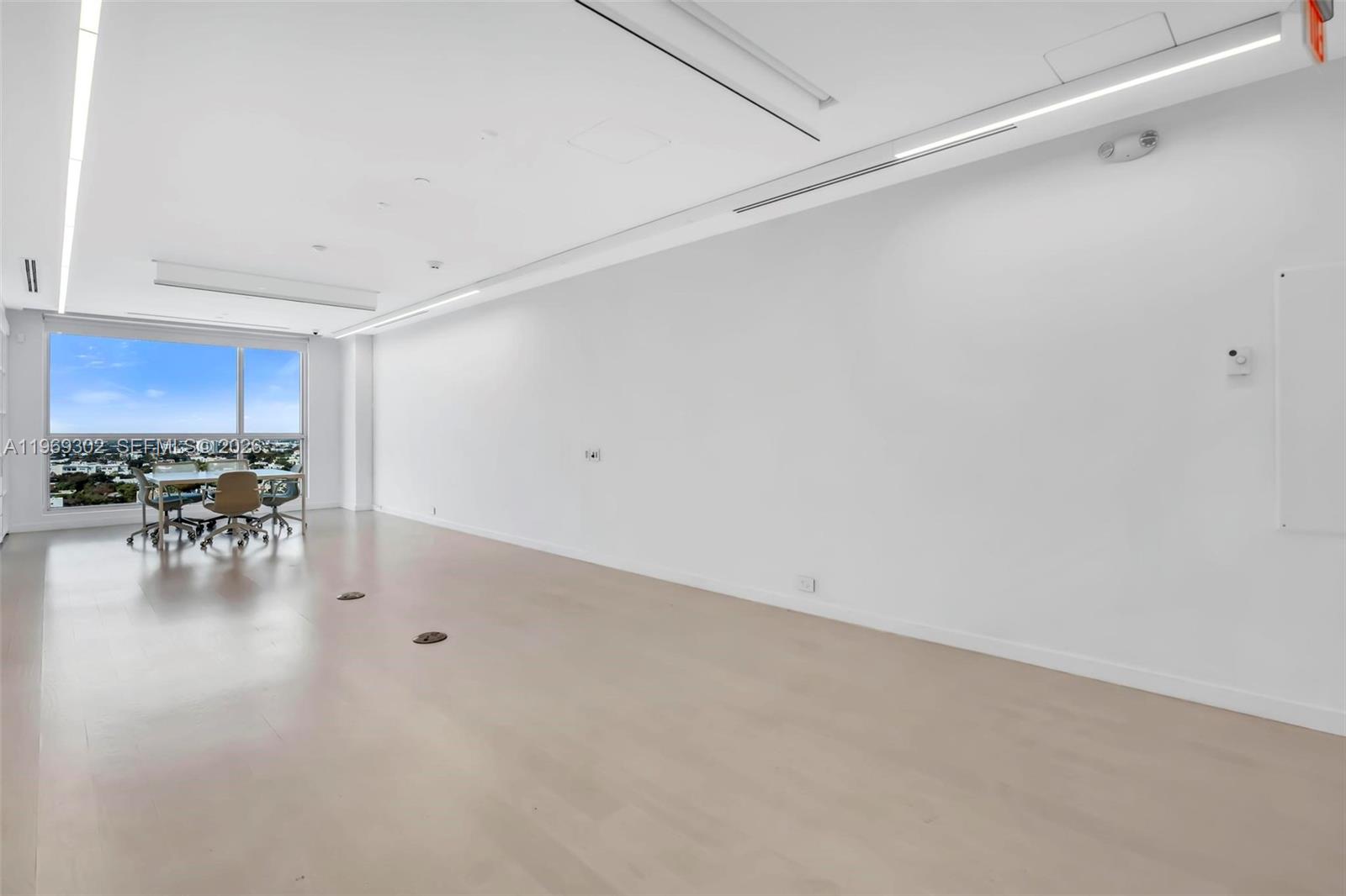 A minimalist office space features light wood flooring, white walls, and a large window view — 175 SW 7th St # 1715, Miami FL 33130, MIAMI, FL