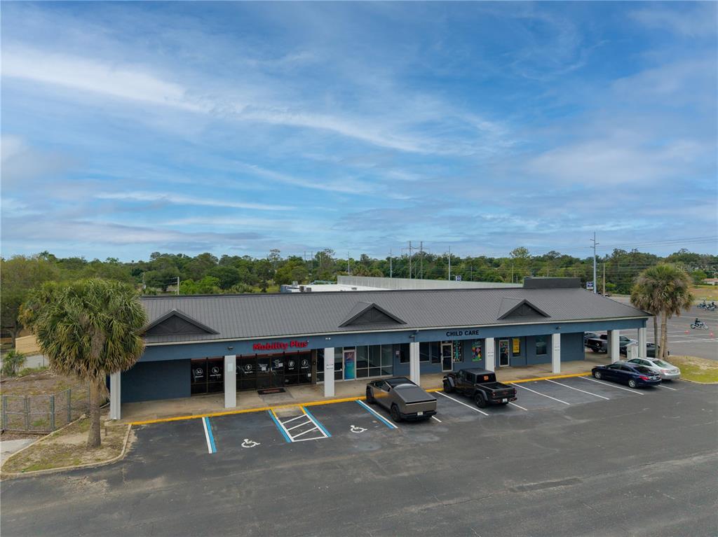An exterior view of a single-story commercial strip mall with a dark metal roof — 9413 SE MARICAMP ROAD, OCALA, FL