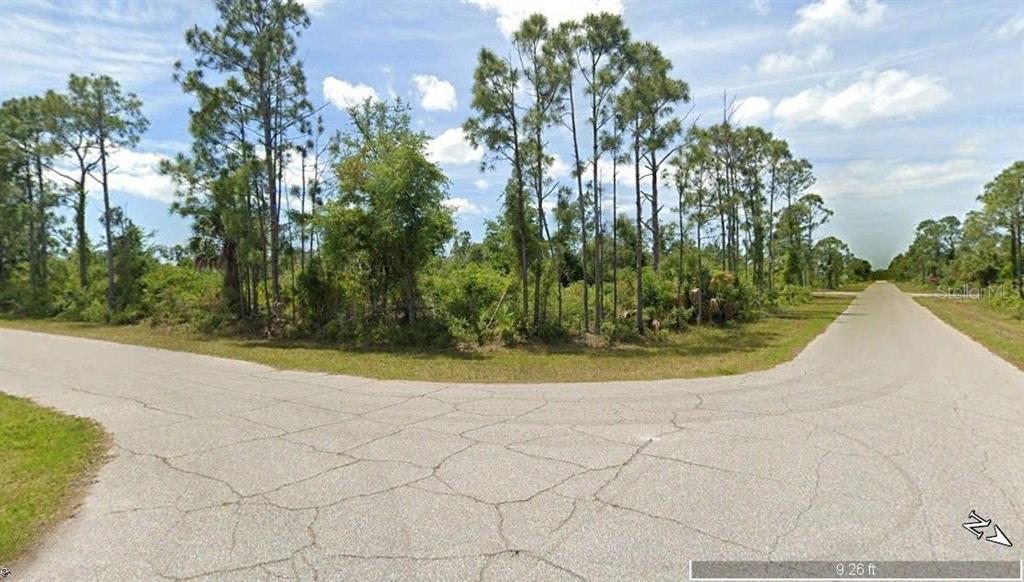A paved road curves past a wooded, undeveloped lot under a blue sky — 12149 BENHAM AVENUE, PORT CHARLOTTE, FL