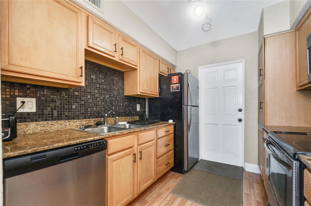 A kitchen features light wood cabinets, granite countertops, a dark tile backsplash, and stainless appliances — 225 E NEW HAMPSHIRE STREET UNIT 7, ORLANDO, FL