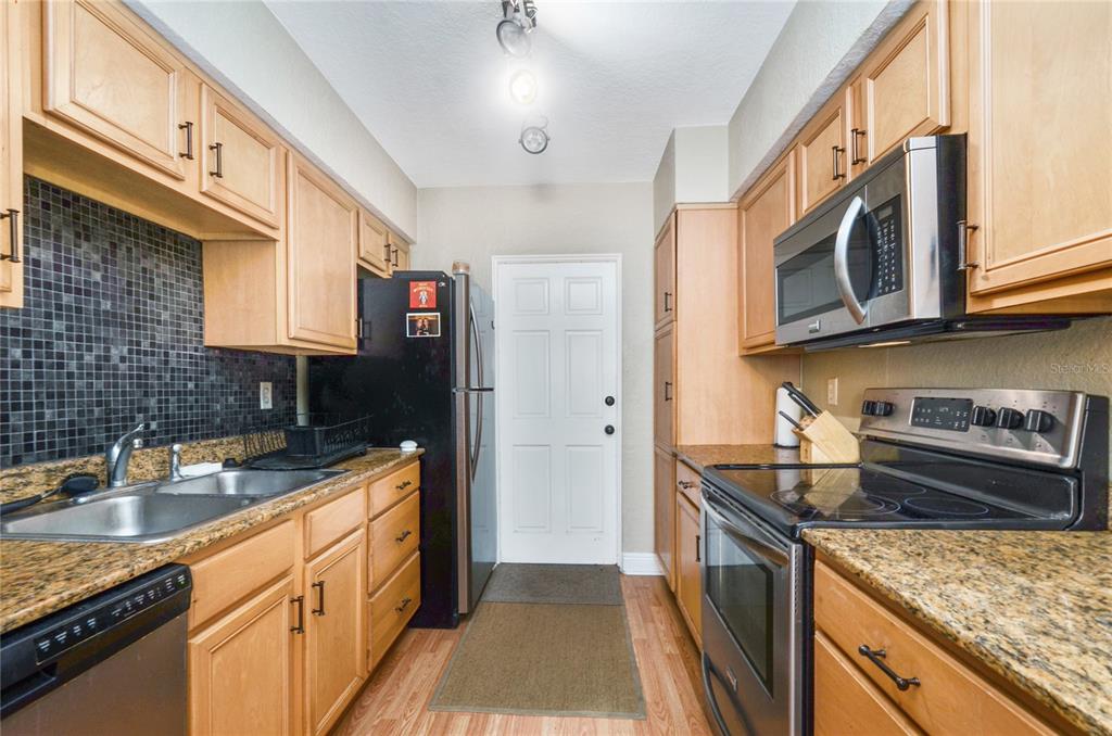 A galley kitchen features light wood cabinets, granite countertops, a black refrigerator, and dark tile — 225 E NEW HAMPSHIRE STREET UNIT 7, ORLANDO, FL