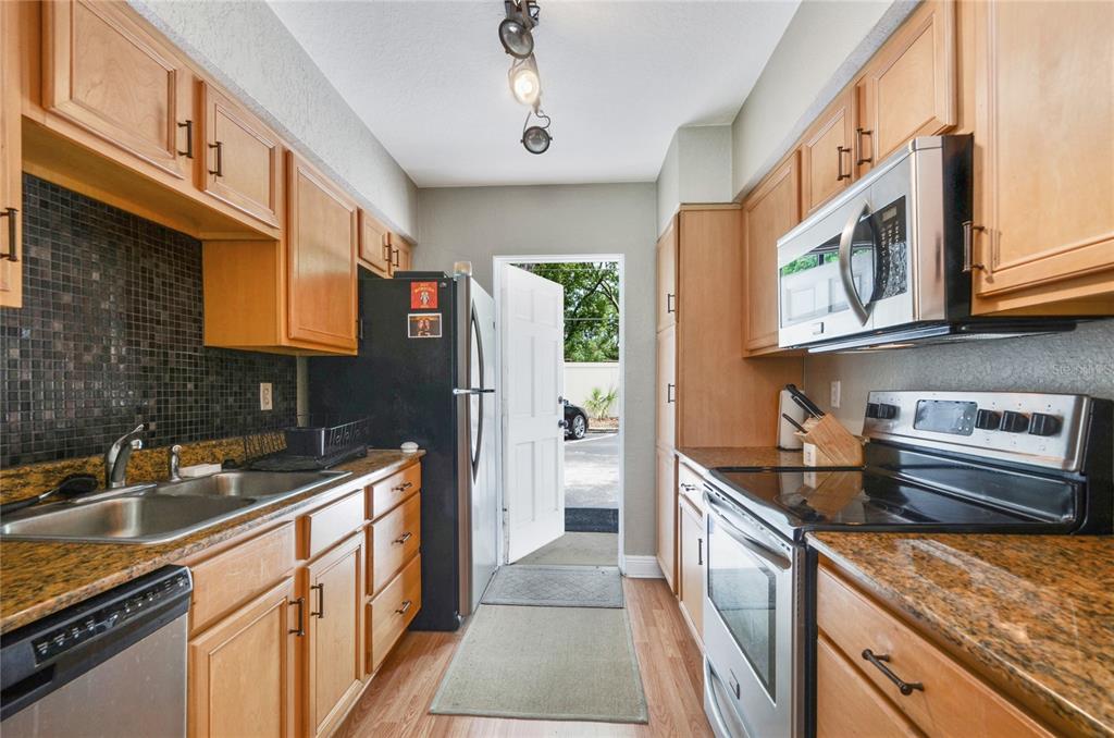 A galley-style kitchen features light wood cabinets, granite countertops, stainless steel appliances, and a doorway — 225 E NEW HAMPSHIRE STREET UNIT 7, ORLANDO, FL