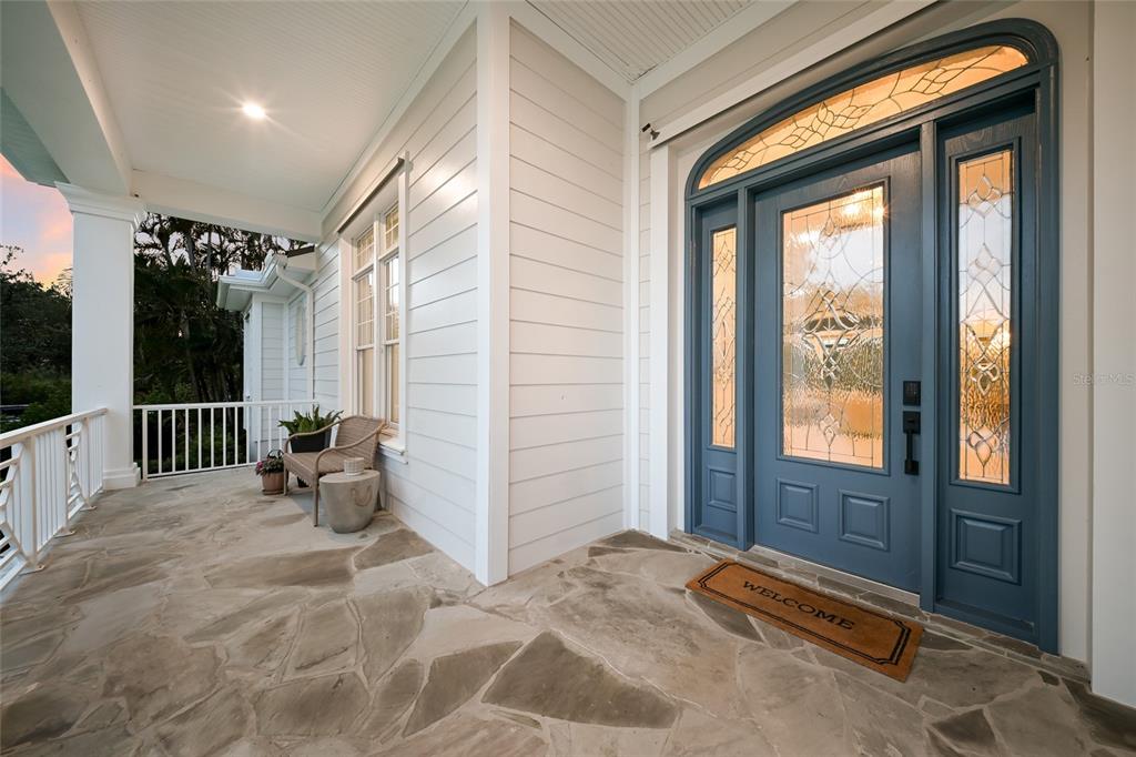 A covered porch features a stone floor, white siding, and a blue front door with glass — 4678 SILENT CREEK WAY, NOKOMIS, FL