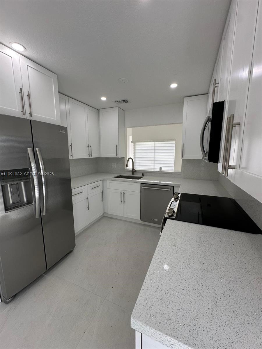 This kitchen features white cabinets, stainless steel appliances, and light-colored quartz countertops — 20926 SW 124th Ave Rd, Miami FL 33177, MIAMI, FL