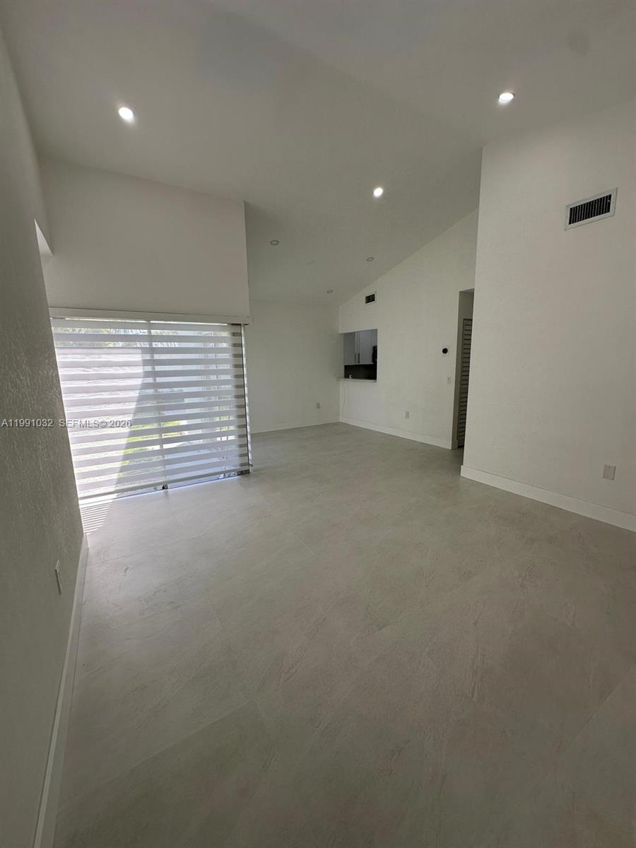 An empty room features white walls, recessed lighting, light-colored tile flooring, and a large window — 20926 SW 124th Ave Rd, Miami FL 33177, MIAMI, FL