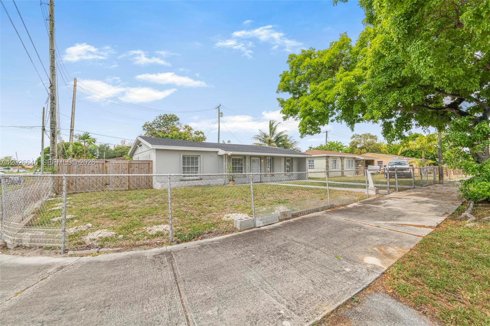A single-story gray house with a chain-link fence sits behind a concrete sidewalk — 1200 NW 87th St # 1, Miami FL 33147, MIAMI, FL